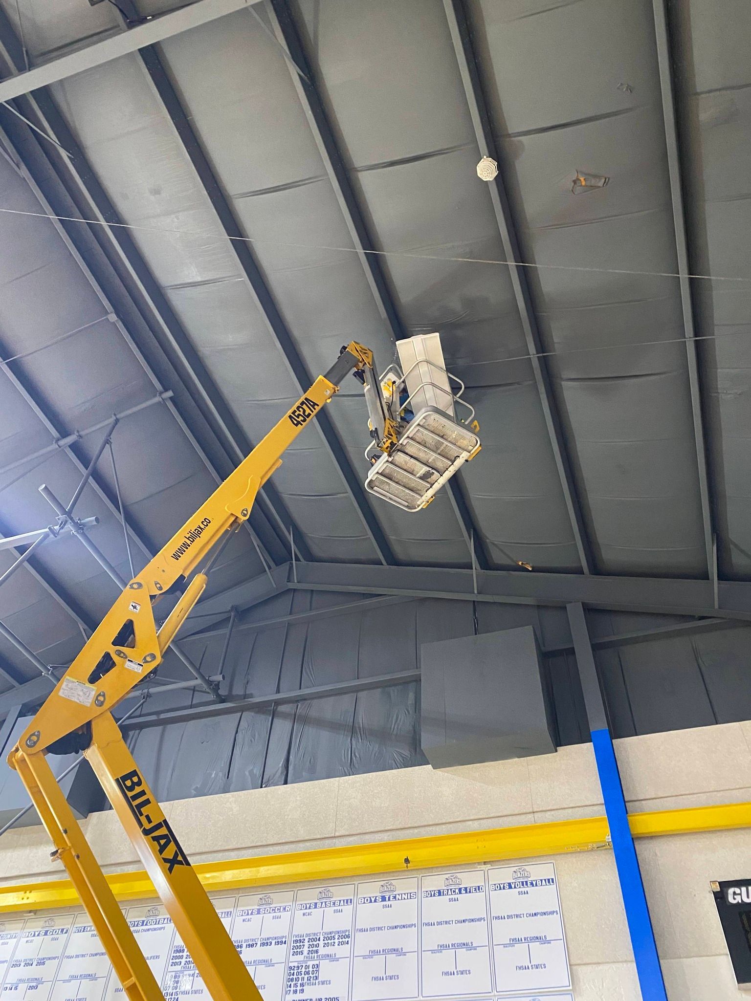 Yellow boom lift raised to a warehouse ceiling with a worker in the basket.