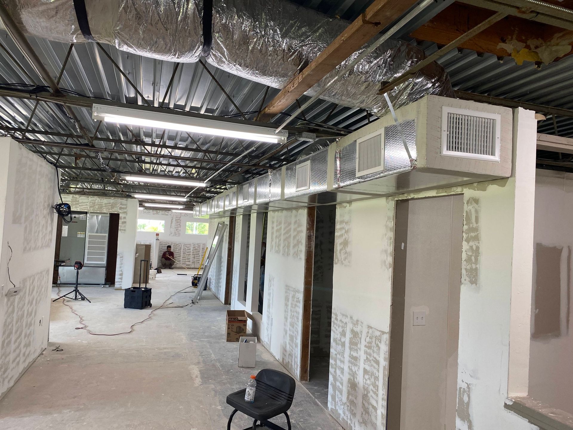 Renovation site with exposed ducts, unfinished walls, and construction materials in a long hallway