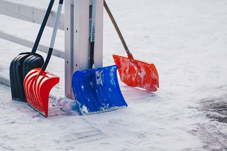 Colorful snow shovels leaning against a post in a snowy outdoor area