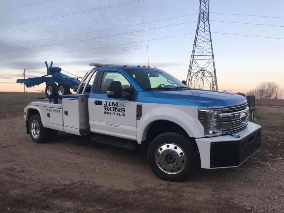 A blue and white tow truck is parked in a dirt field.