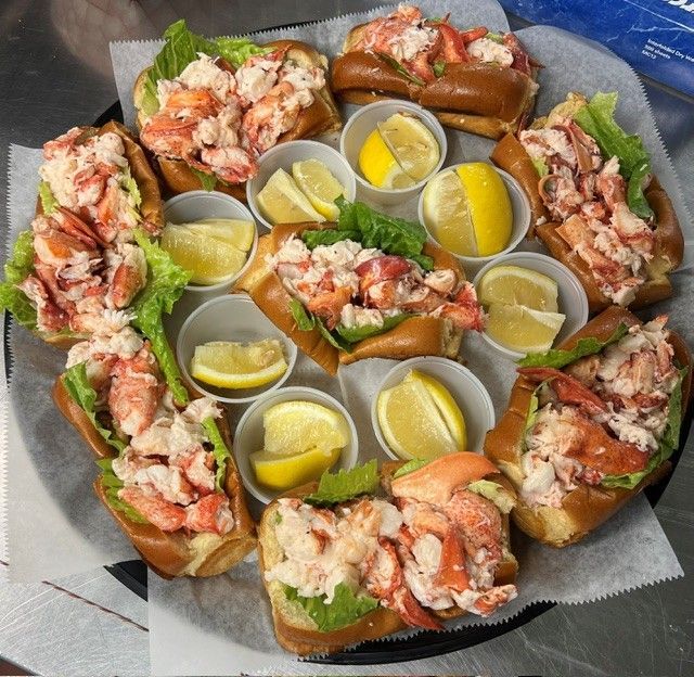 Lobster rolls arranged on a tray with lemon wedges and dipping cups.