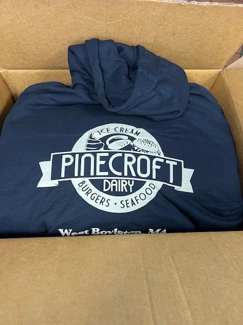 Dark blue Pinecroft Dairy hoodie in a cardboard box.