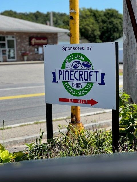Sign for Pinecroft Dairy, sponsored sign, pointing right, 1/2 mile. Burgers, seafood, and ice cream available.