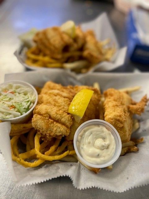 Fried fish platter with coleslaw, fries, and tartar sauce. A slice of lemon sits on top.
