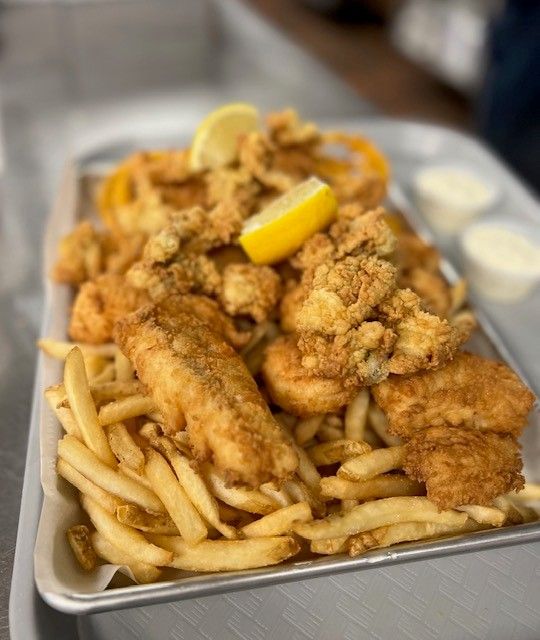Fried seafood platter with fries, lemon wedges, and dipping sauces on a metal tray.