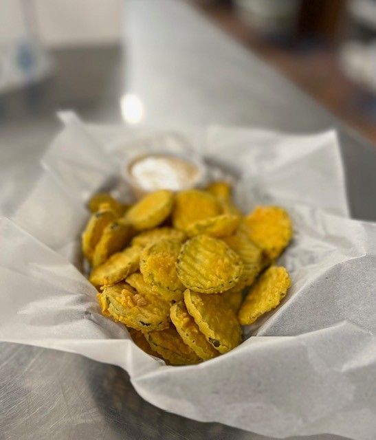 Fried pickle chips in a basket with dipping sauce, on a paper liner, on a counter.