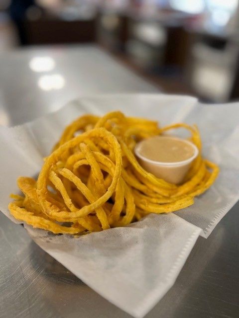 Curly fries with dipping sauce in a white paper-lined basket on a reflective surface.