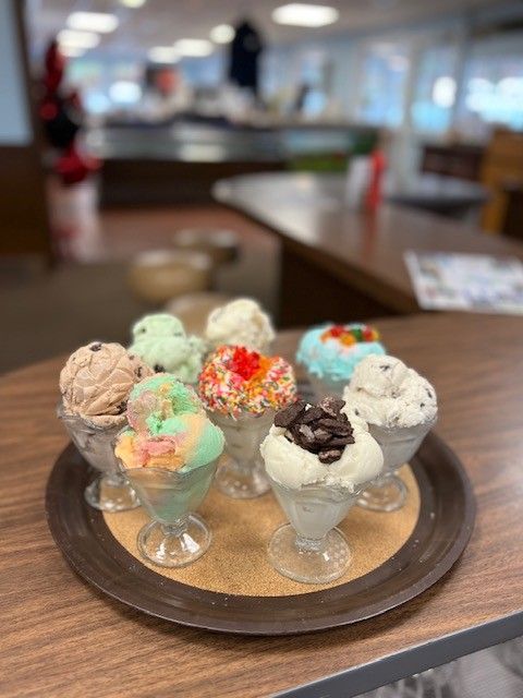 A tray with eight scoops of various ice cream flavors in clear glass dishes, on a table.