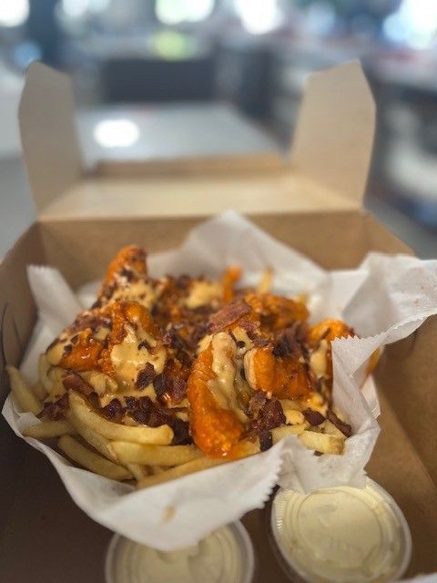 Fries with cheese sauce, bacon, in a cardboard box, with dipping sauces.