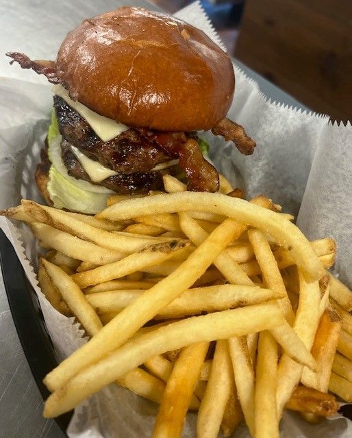 Burger with cheese and bacon, served with a pile of french fries in a basket.