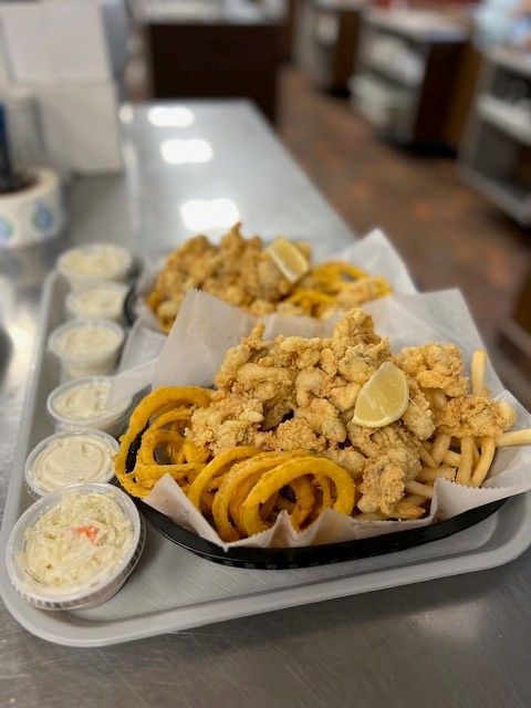 Fried seafood baskets with curly fries, coleslaw, and dipping sauces on a tray.