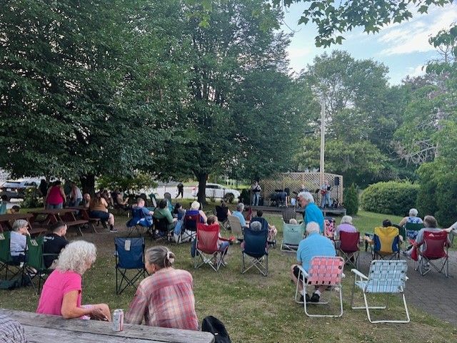 A group of people are sitting in chairs in a park watching a concert.