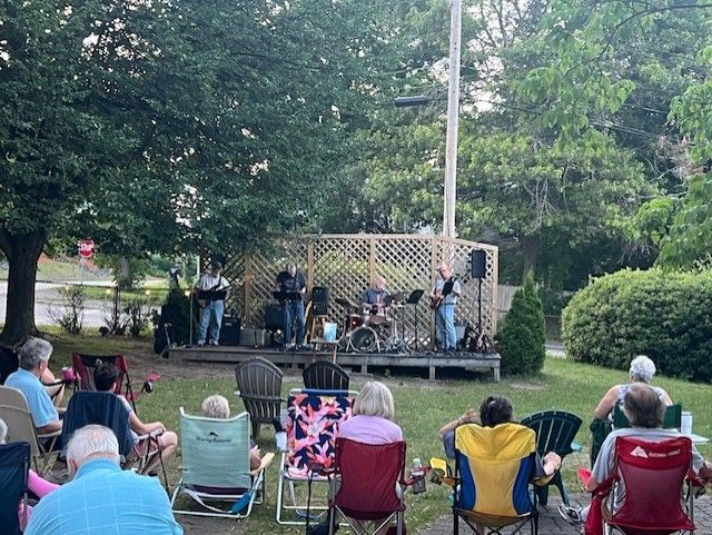 A group of people are sitting in chairs in front of a stage watching a band perform.