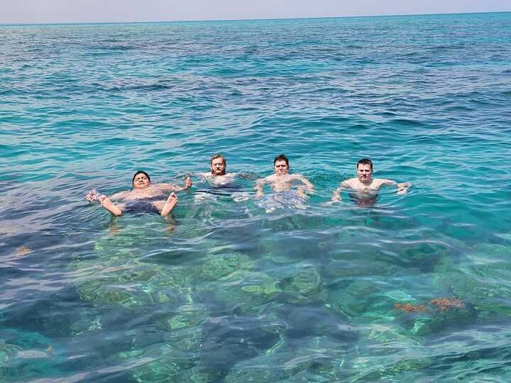 Four people swimming in clear blue ocean water near a rocky reef.
