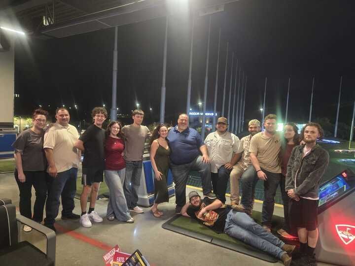 Group of people at night at a Topgolf, posing near the mats and golf targets.