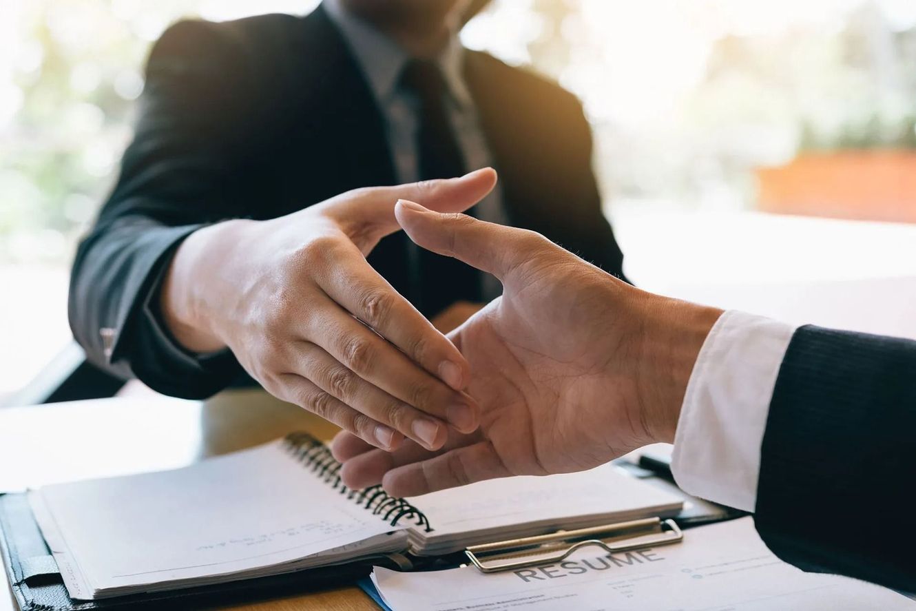 Two people in suits shaking hands over an open notebook, signifying agreement or deal.