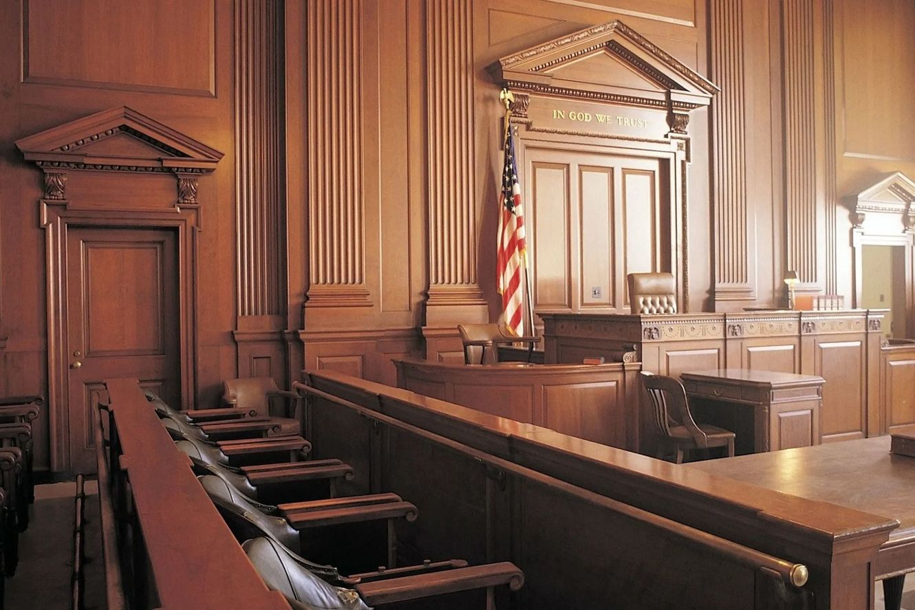 Empty courtroom interior with wooden paneling, judge's bench, and the American flag.