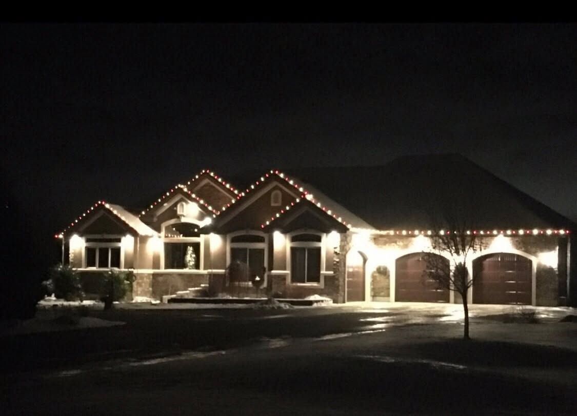 Snowy suburban house at night, lit with white Christmas lights and a two-car garage.