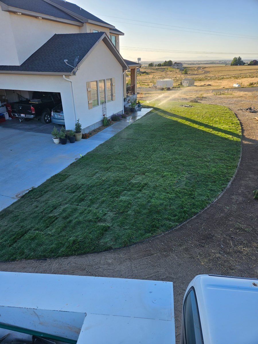 Suburban house with a green lawn and curved dirt driveway at sunset, overlooking open fields