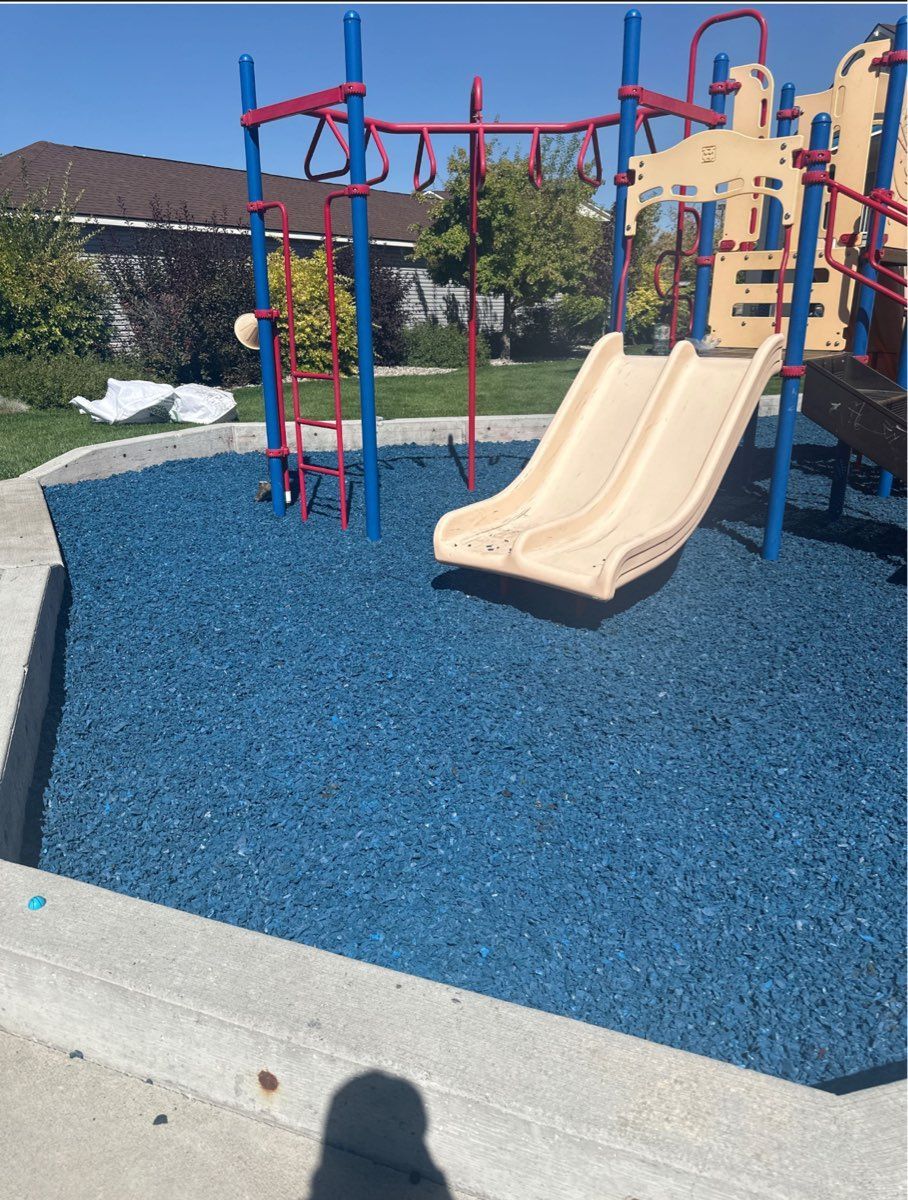 Playground with blue rubber ground, beige slides, and red climbing bars under a clear sky