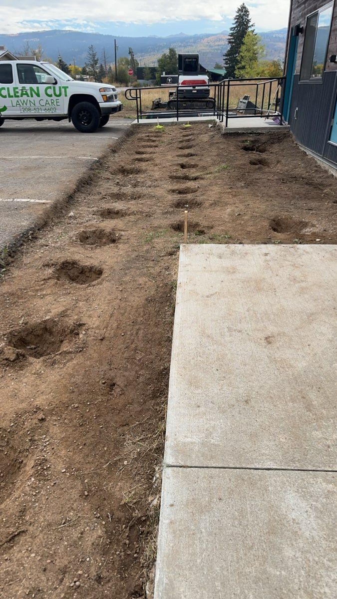 Freshly dug dirt path with circular holes beside a concrete walkway and a utility truck in the background