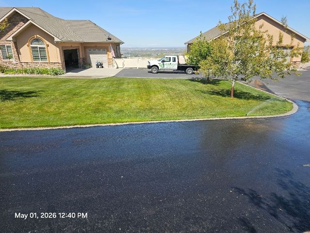 Suburban driveway and lawn in front of houses on a sunny day, with a white truck parked near a garage.