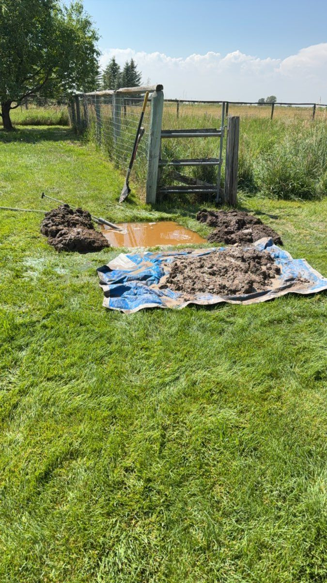 Blue tarp and mud-covered boards on grass near a wooden gate in a fenced field