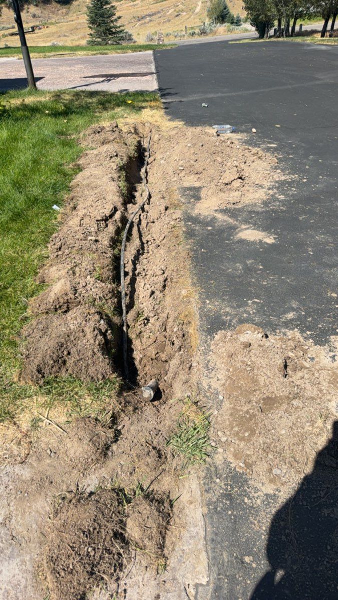 Cracked asphalt road with a deep erosion trench along the edge beside a grassy area.
