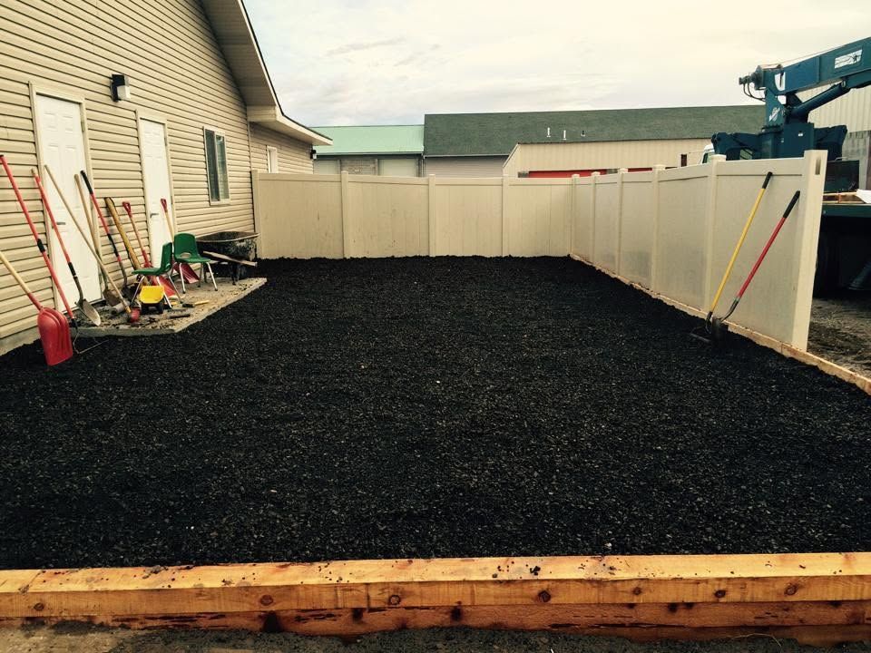 Freshly graveled backyard beside a house, with fences and tools along the side yard.
