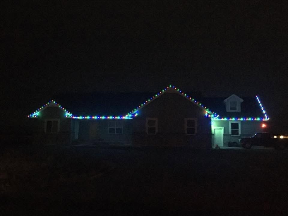 House at night outlined with multicolored holiday lights, with a bright porch light at the entrance