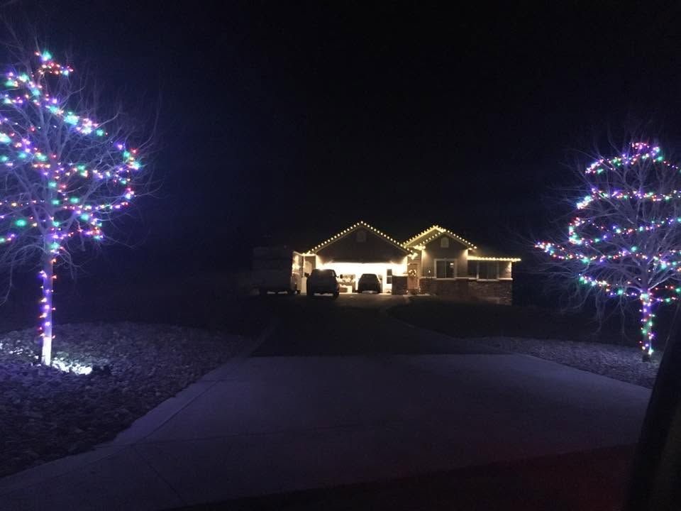 Lit house at night framed by two trees wrapped in colorful holiday lights