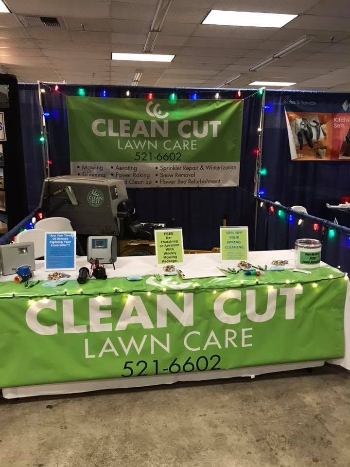 CLEAN CUT Lawn Care booth with green banners, table display, and string lights at an indoor expo.