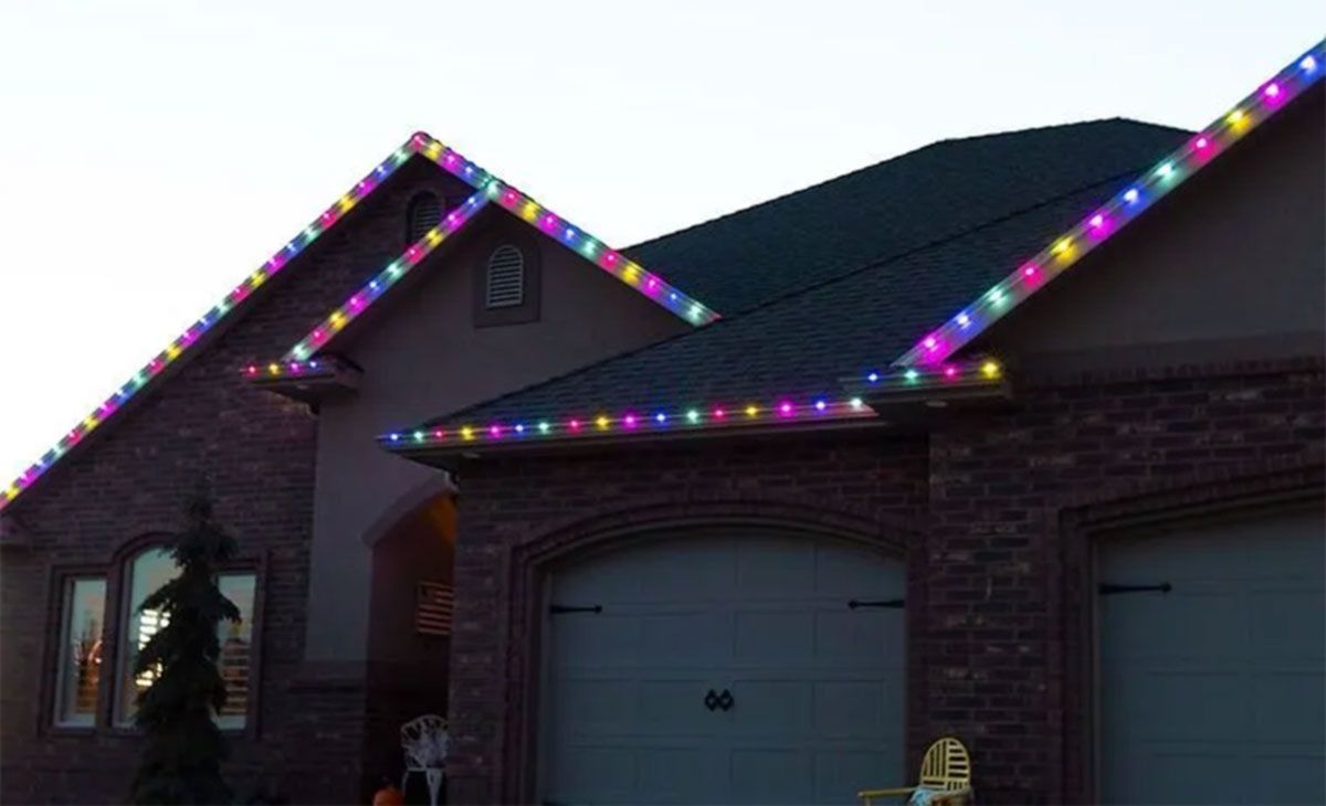 House at dusk with multicolored Christmas lights along the roofline and gables