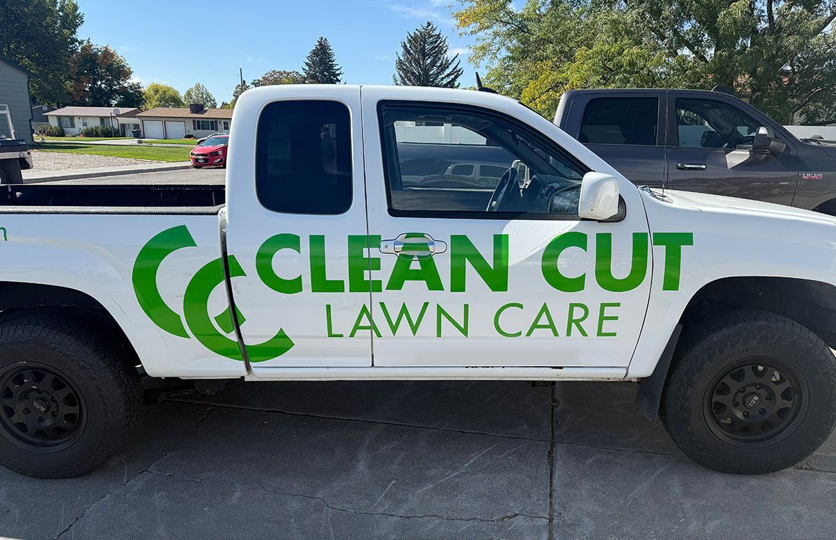 White pickup truck with green “Clean Cut Lawn Care” logo parked on a sunny street