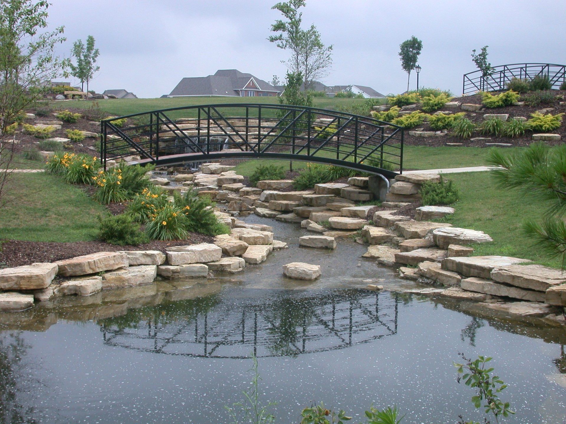 A bridge over a pond with a house in the background