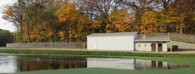 A white building is sitting next to a pond with trees in the background.