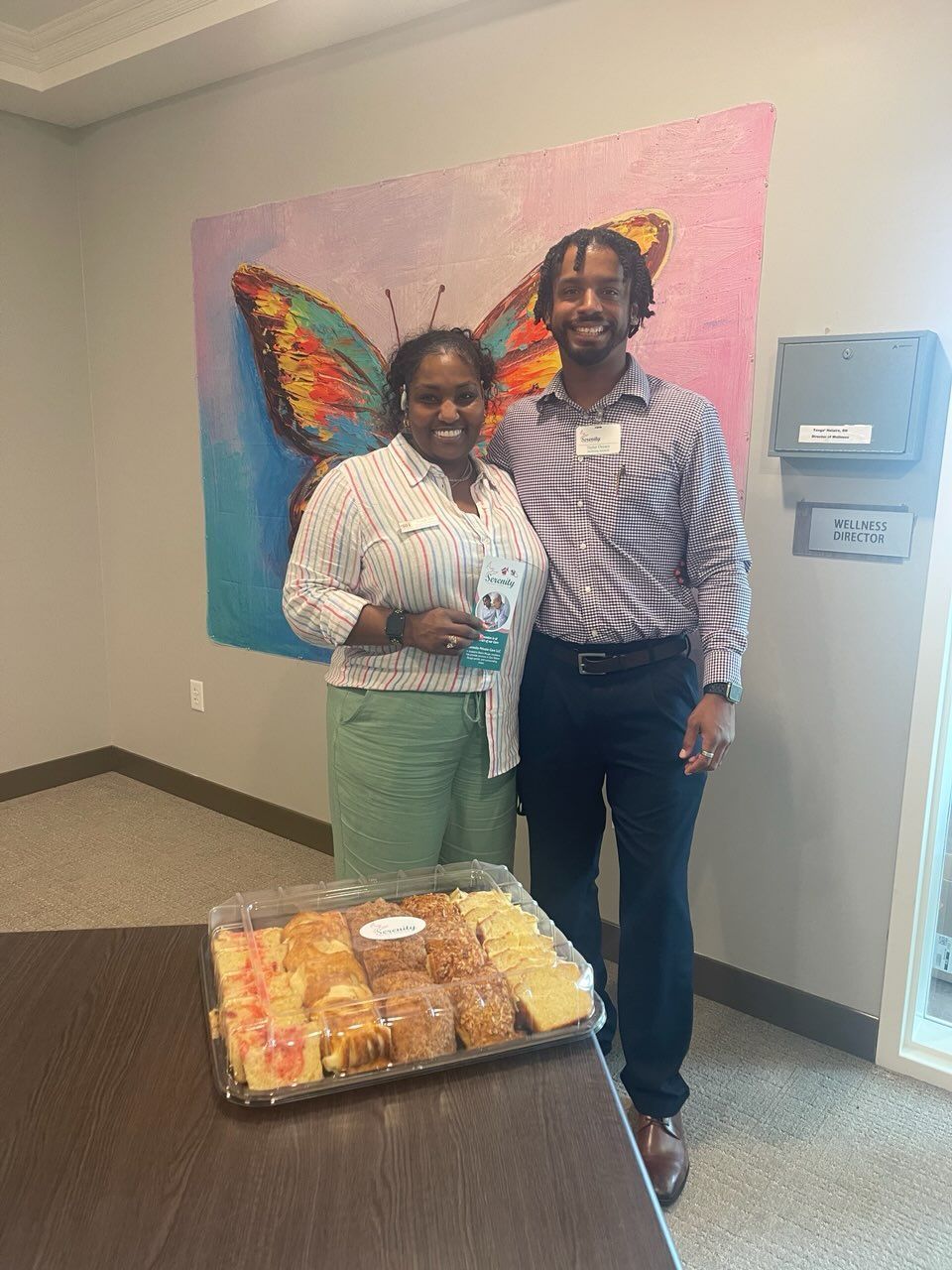 A man and a woman are standing next to a table with a tray of food.