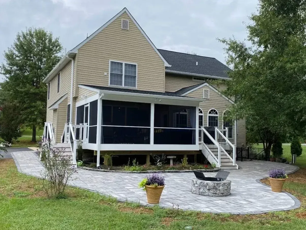 Backyard patio with a beige house, screened porch, stone pavers, and potted plants