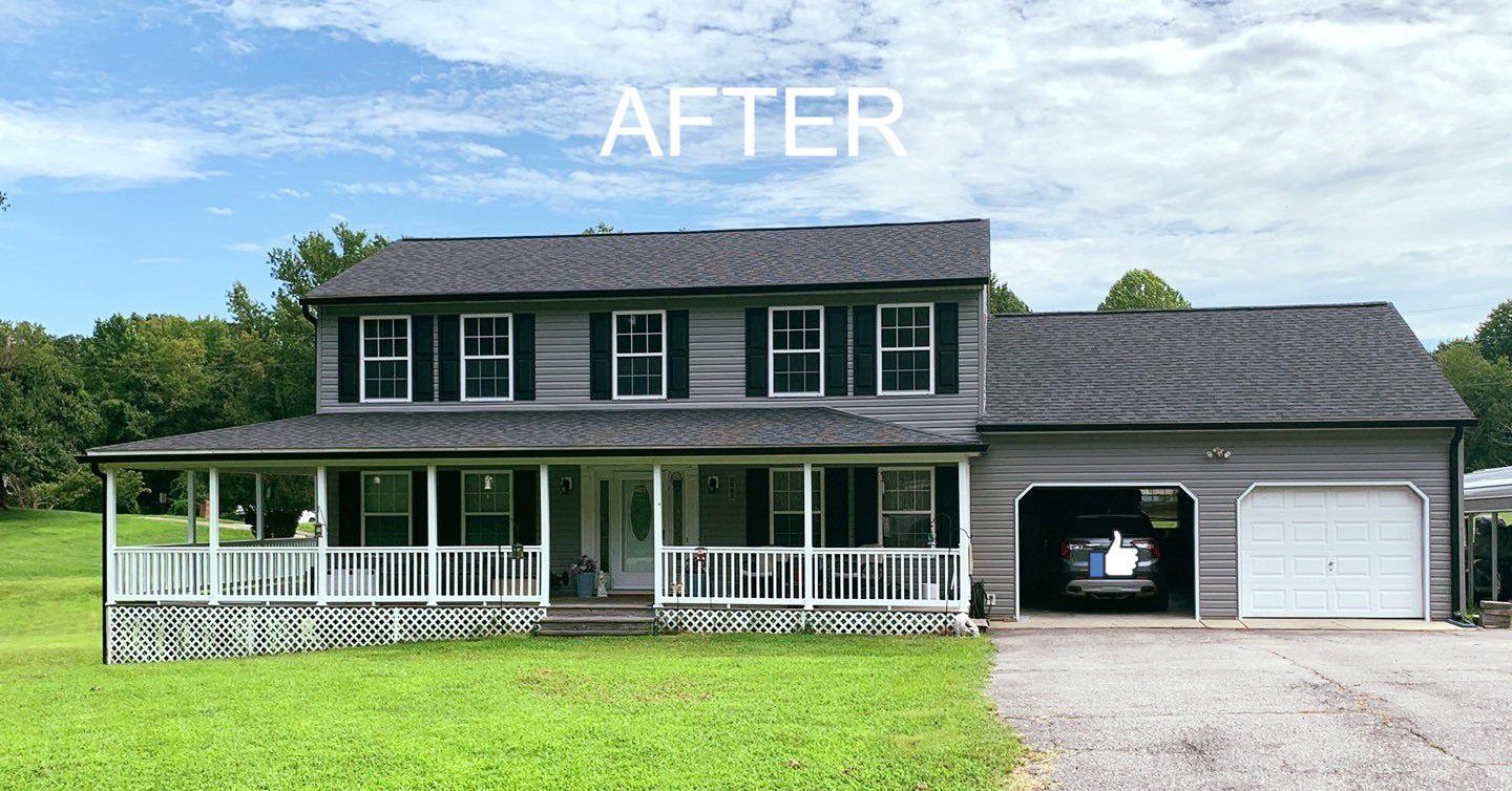 Two-story gray house with white porch, green lawn, and detached garage under a blue sky