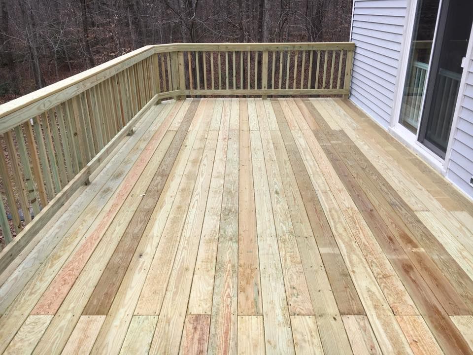Wooden deck with pale boards and railings beside a house, overlooking a wooded yard.