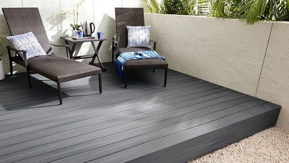 Modern patio with gray deck, two lounge chairs, and a small table by a planter wall.