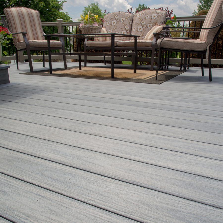 Outdoor patio with cushioned chairs and a table on a gray wooden deck, with greenery in the background