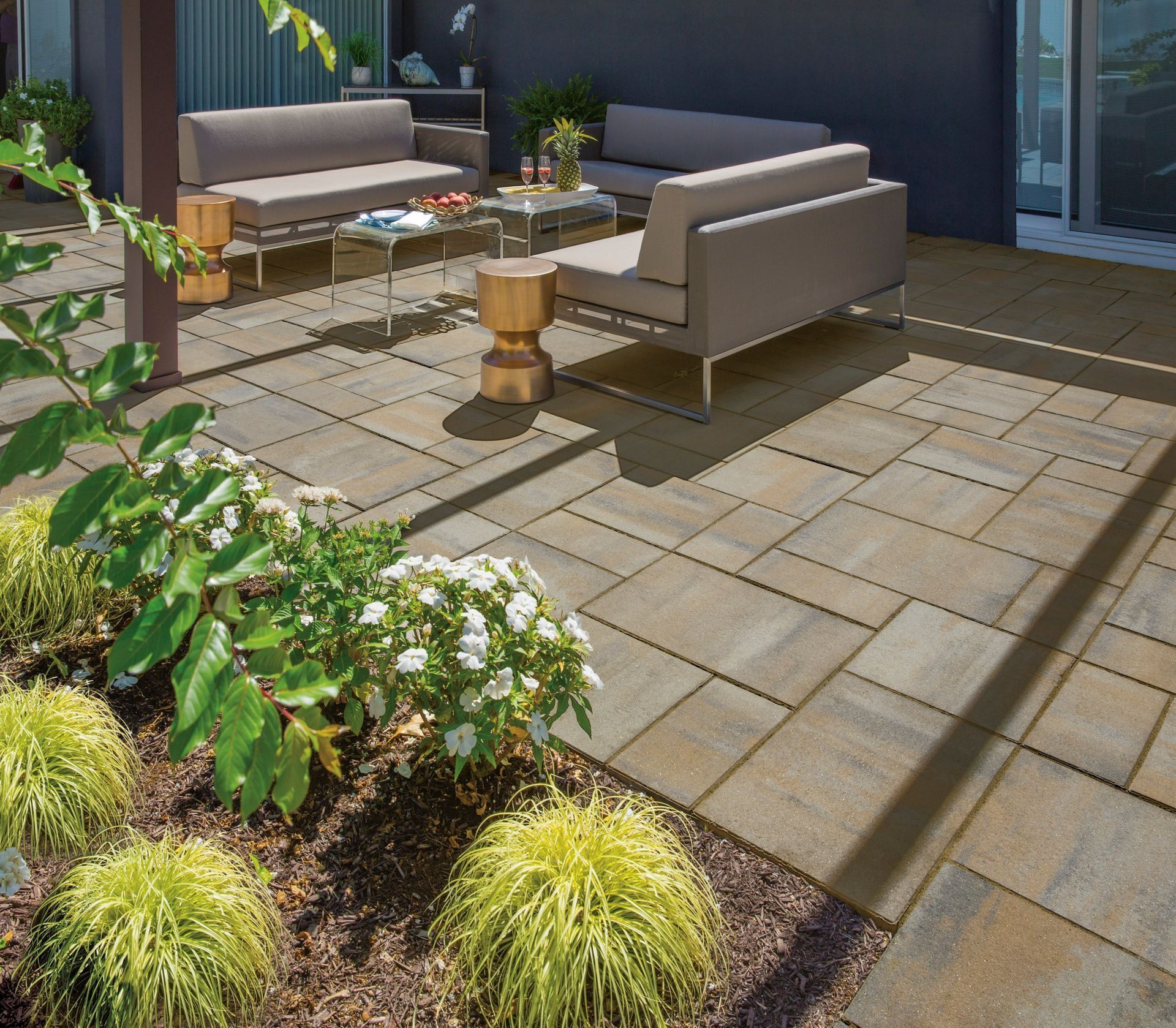 Modern patio with gray outdoor sofas, a small table, and landscaped plants in sunlight