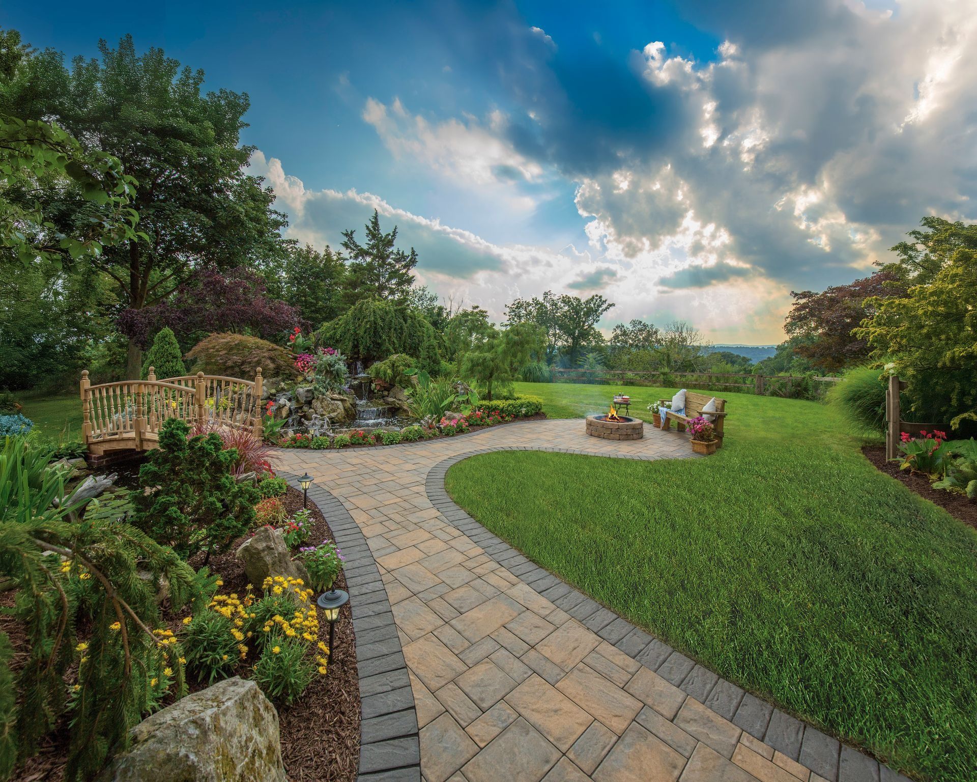 Curved stone garden path through lush greenery toward a patio under a partly cloudy sky