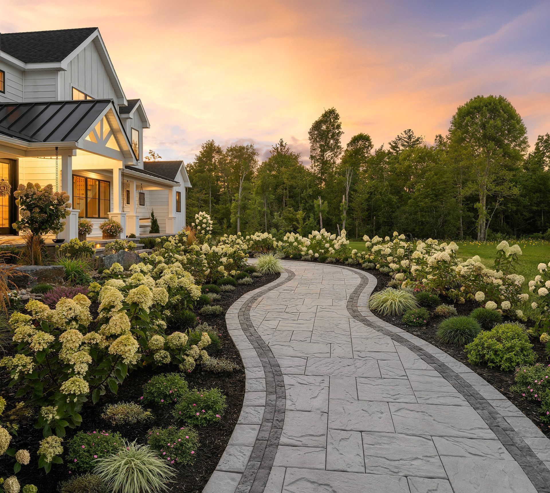 Curved stone garden path beside a house and blooming shrubs at sunset