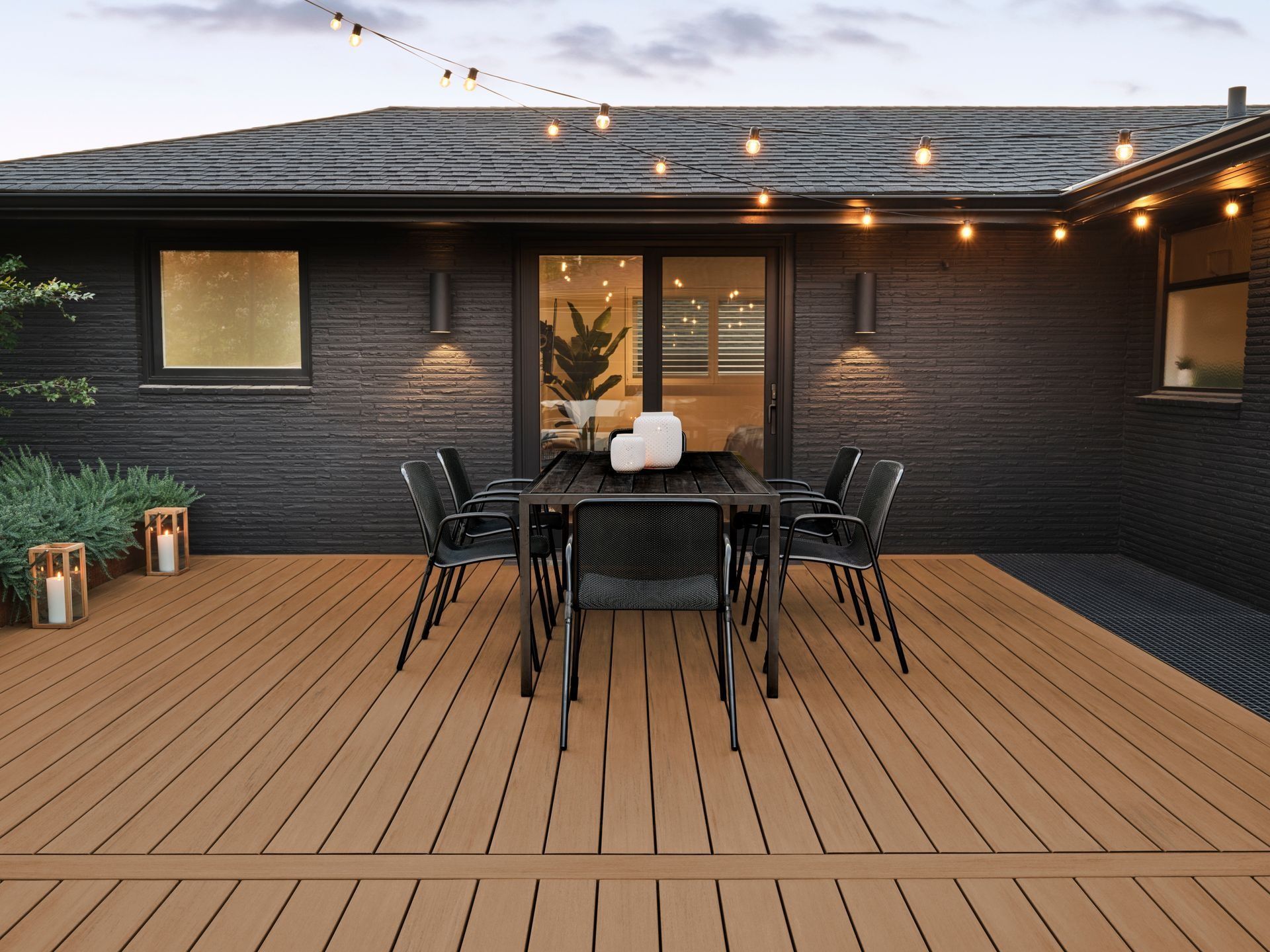 Outdoor patio with a black dining set, string lights, and wood decking against a dark brick house.