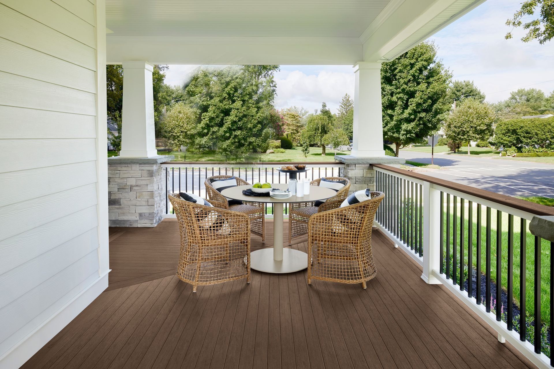 Covered porch with wicker chairs, round table, and view of a green yard and parking lot