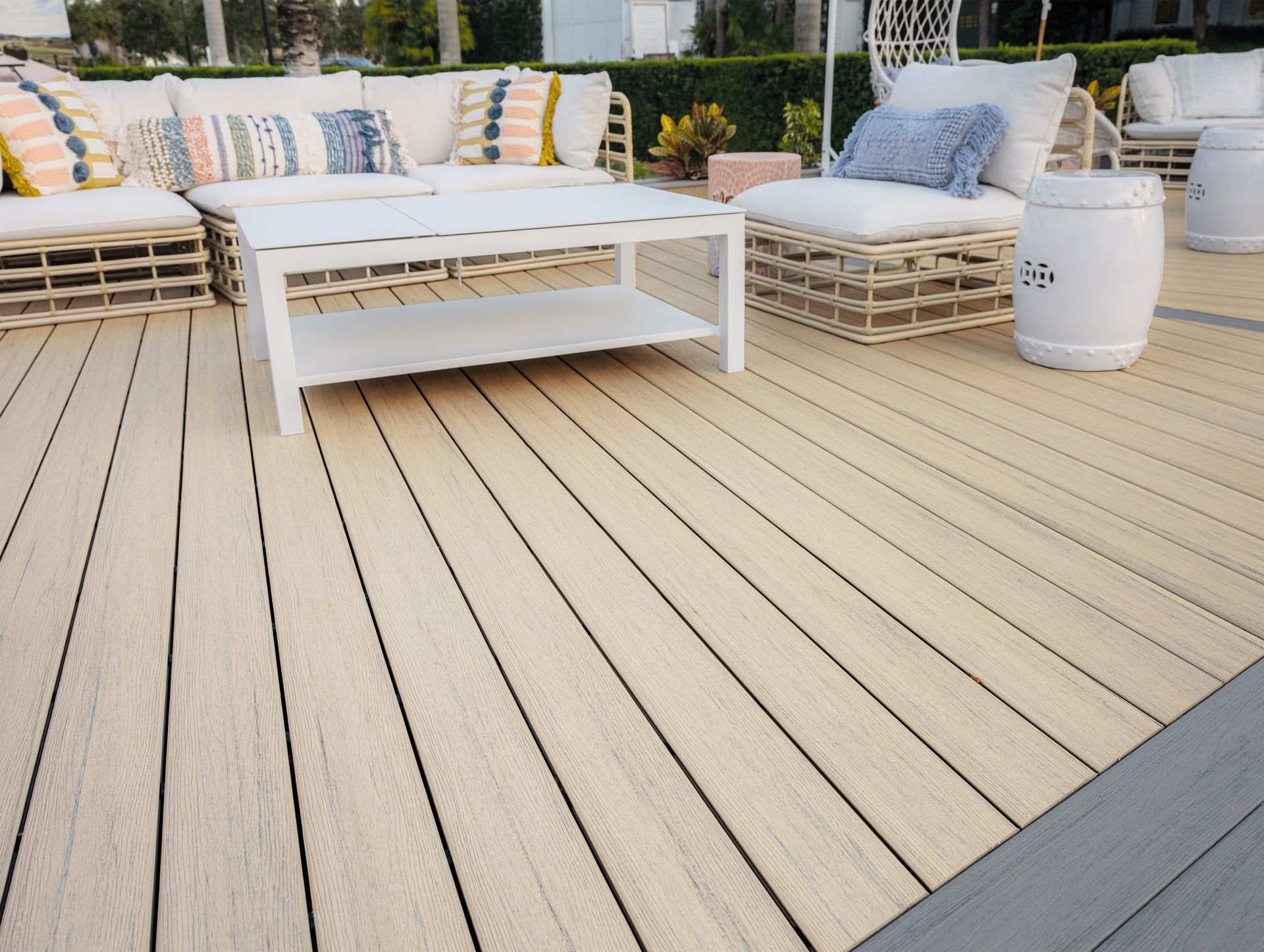 Outdoor patio with white cushioned seating, low coffee table, and beige deck flooring in bright sunlight