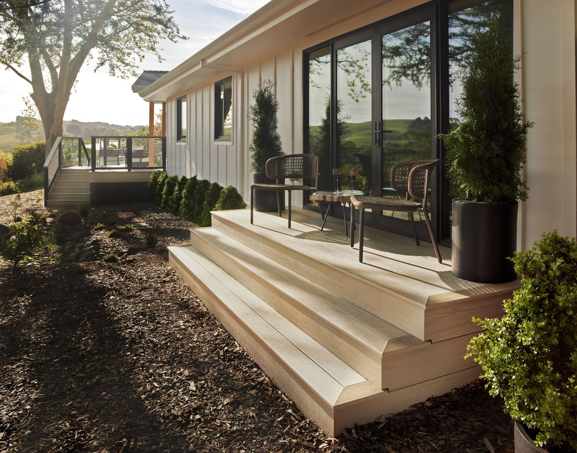 Modern house patio with wide steps, glass doors, potted plants, and a sunlit garden view