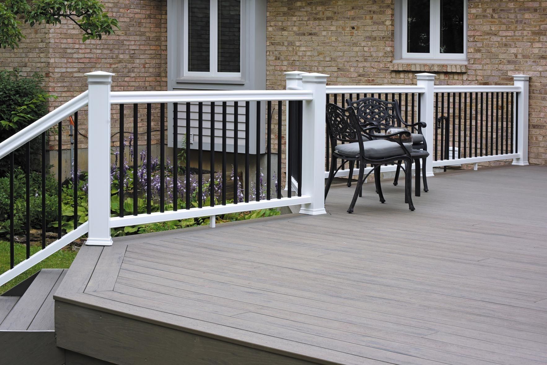Outdoor deck with white railings, black chairs, and a brick house wall